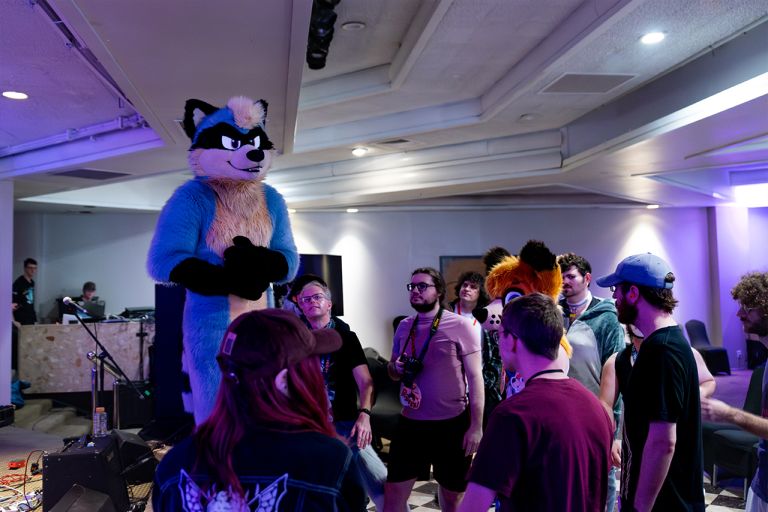 A group of fursuiters standing around, one blue raccoon is standing taller than the rest